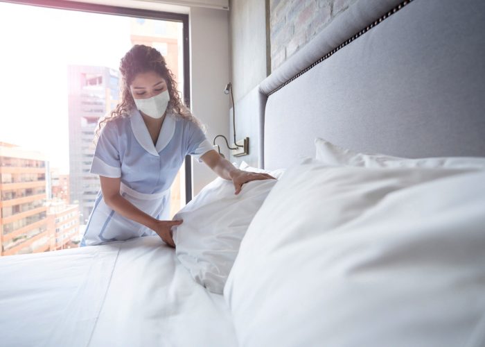 Maid working at a hotel and doing the bed wearing a facemask