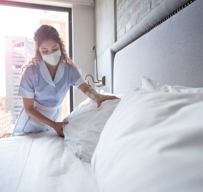 Maid working at a hotel and doing the bed wearing a facemask